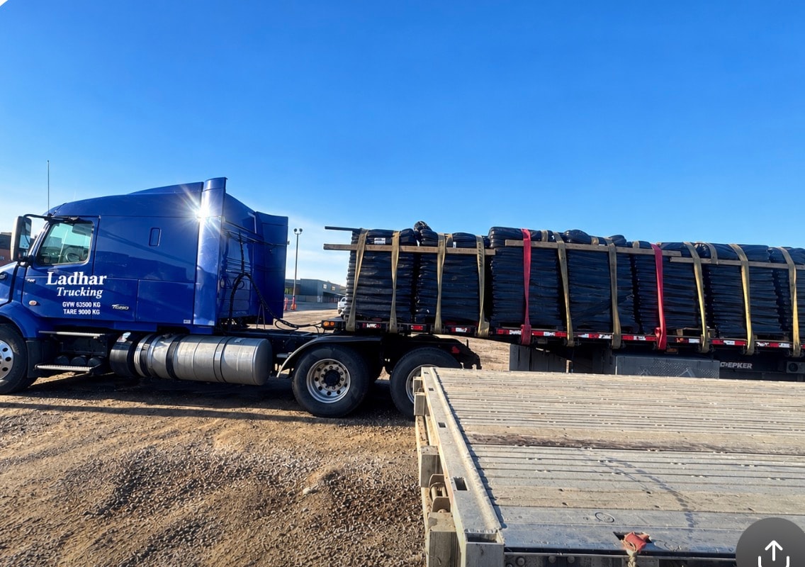 Ladhar Trucking blue semi-truck loaded with tires on flatbed trailer at industrial yard